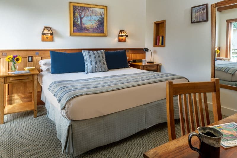 A hotel bedroom featuring a bed with a blue and white striped throw, a wooden headboard with built-in lamps.
