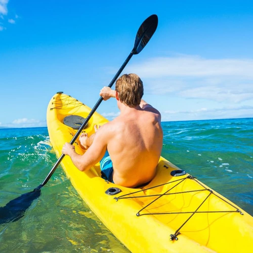A man paddles a yellow kayak in clear blue water under a sunny sky.