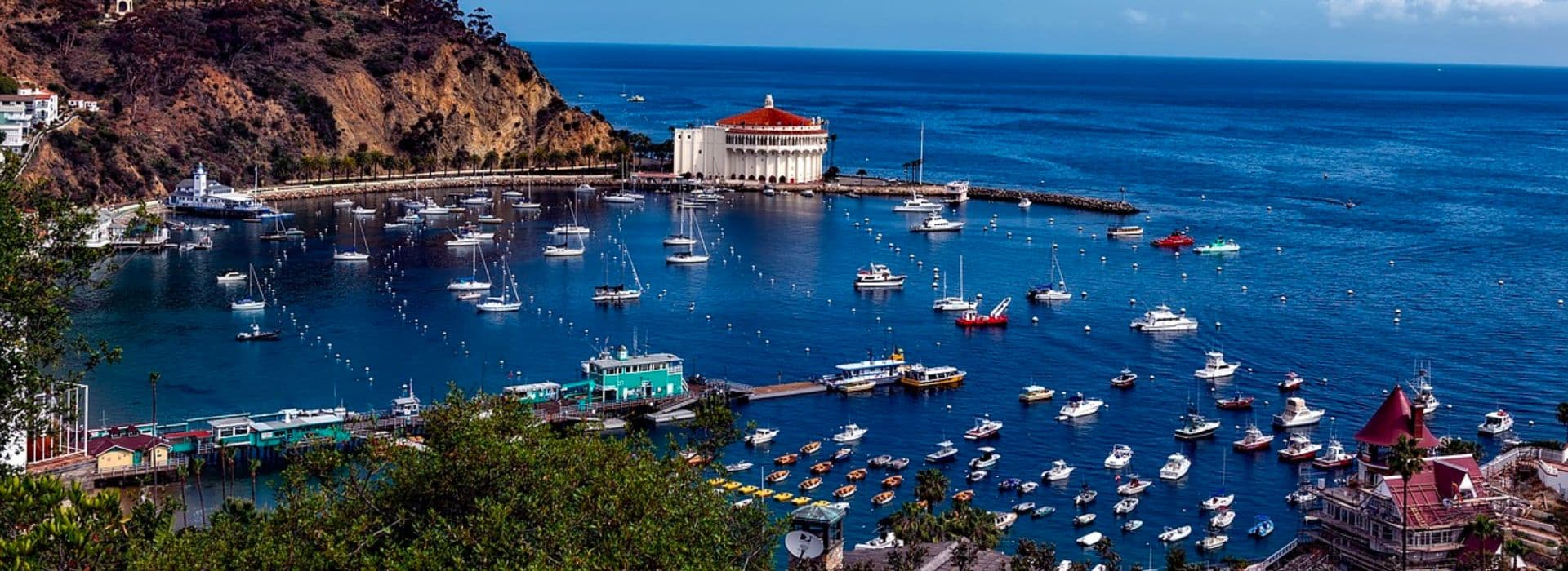 A scenic view of a harbor filled with boats, surrounded by hills and coastal buildings under a clear blue sky.