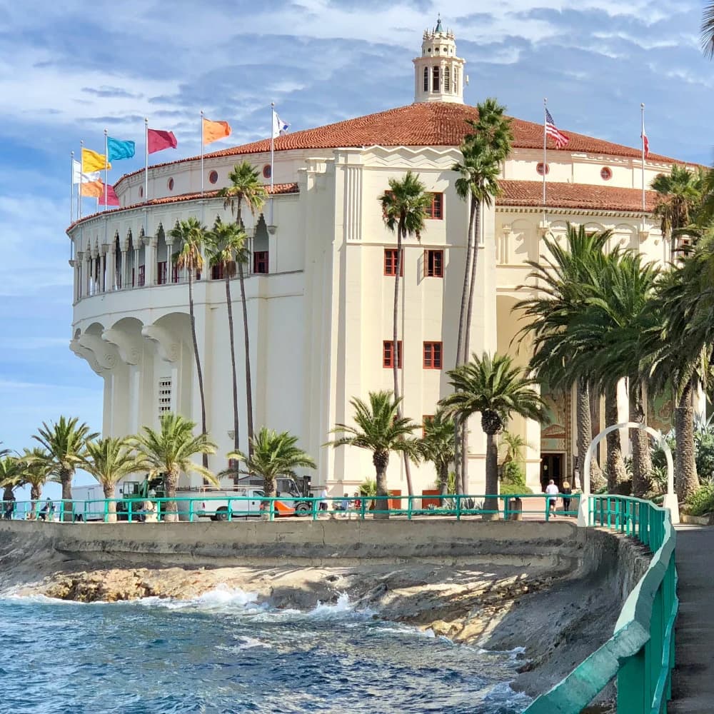 The Casino Building in Avalon, California, surrounded by palm trees and colorful flags.