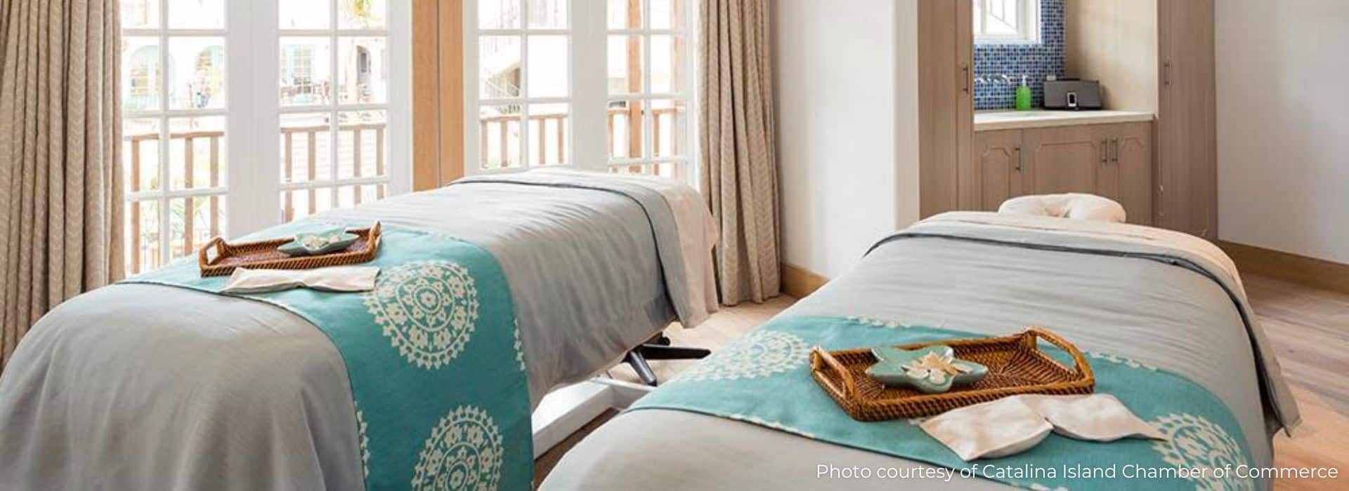 A serene spa room featuring two massage tables adorned with turquoise blankets and decorative trays.