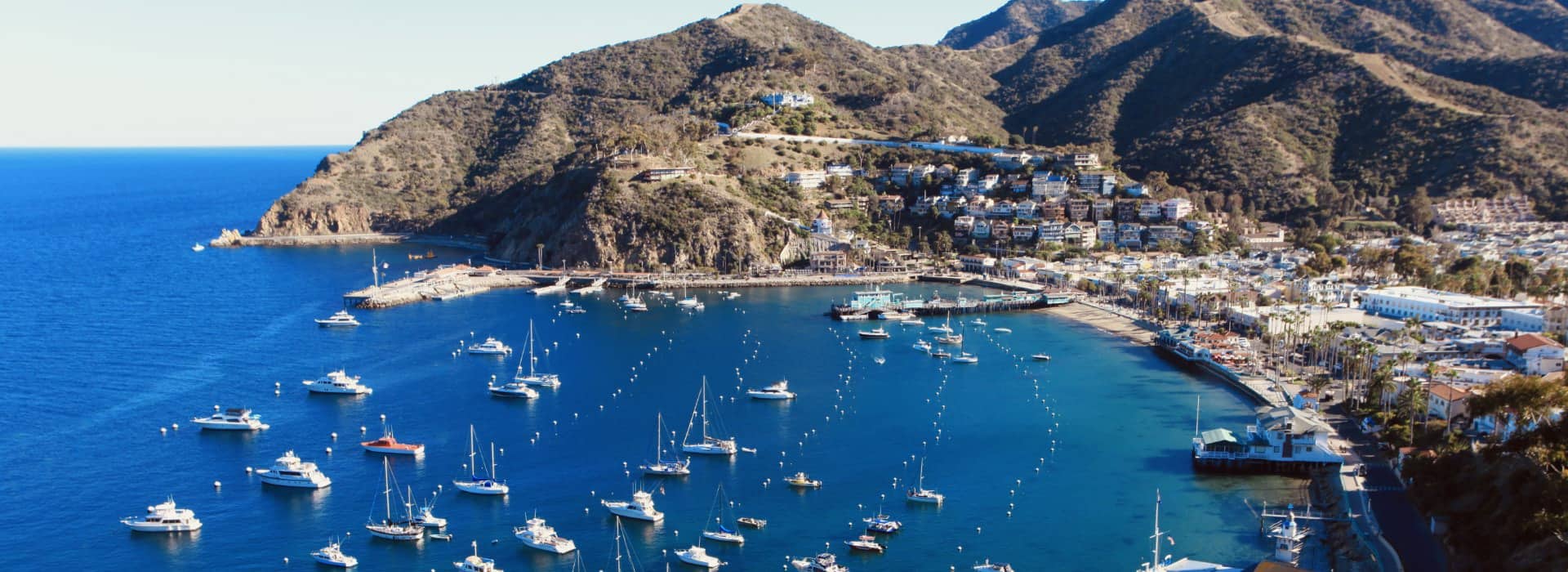 Aerial view of a coastal town with boats docked in the harbor and mountains in the background.
