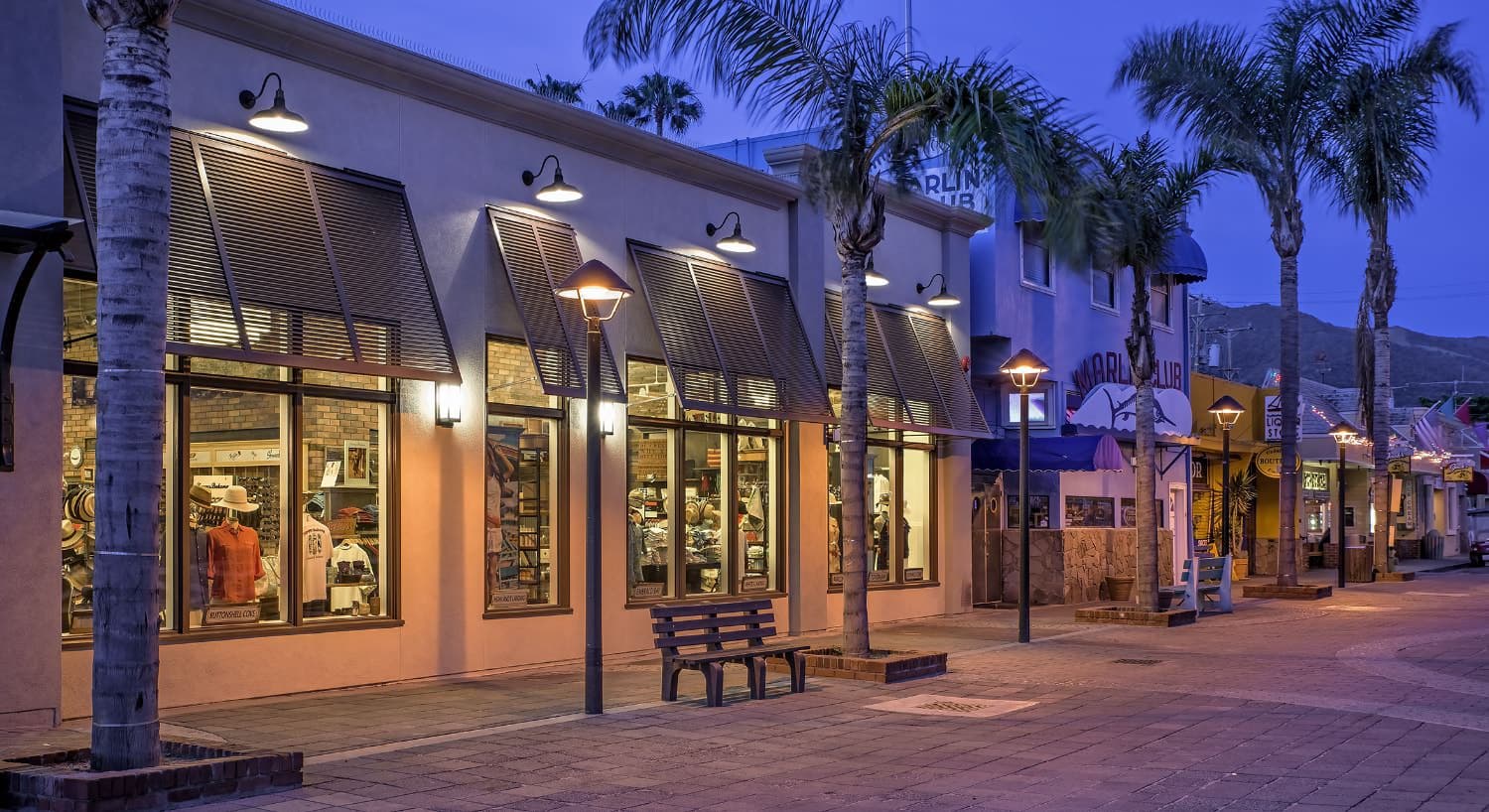 Beach front full of retail and lodging businesses surrounded by palm trees and hills in the background