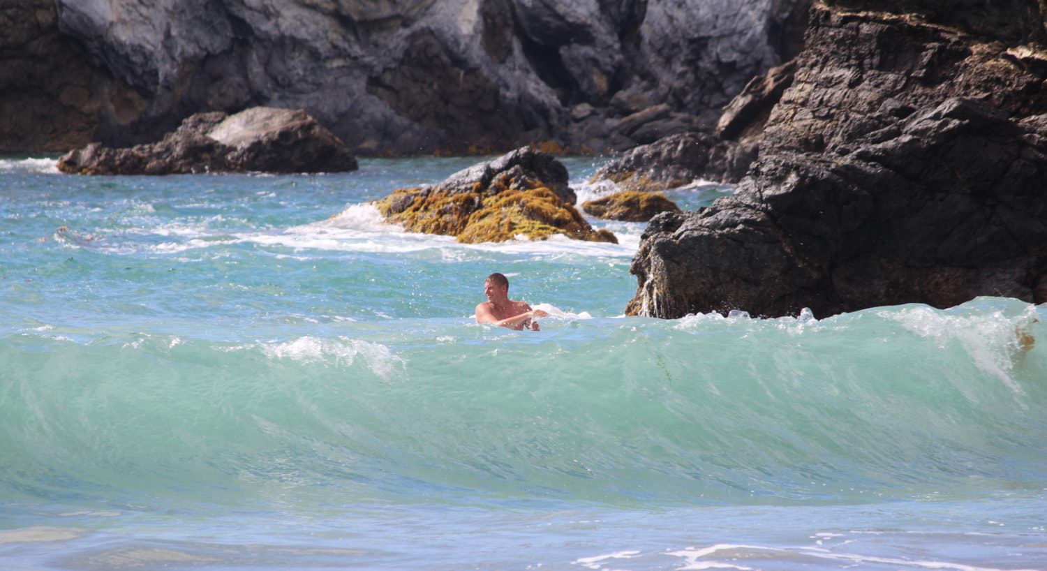 Man playing in the surf with large rocks in the background