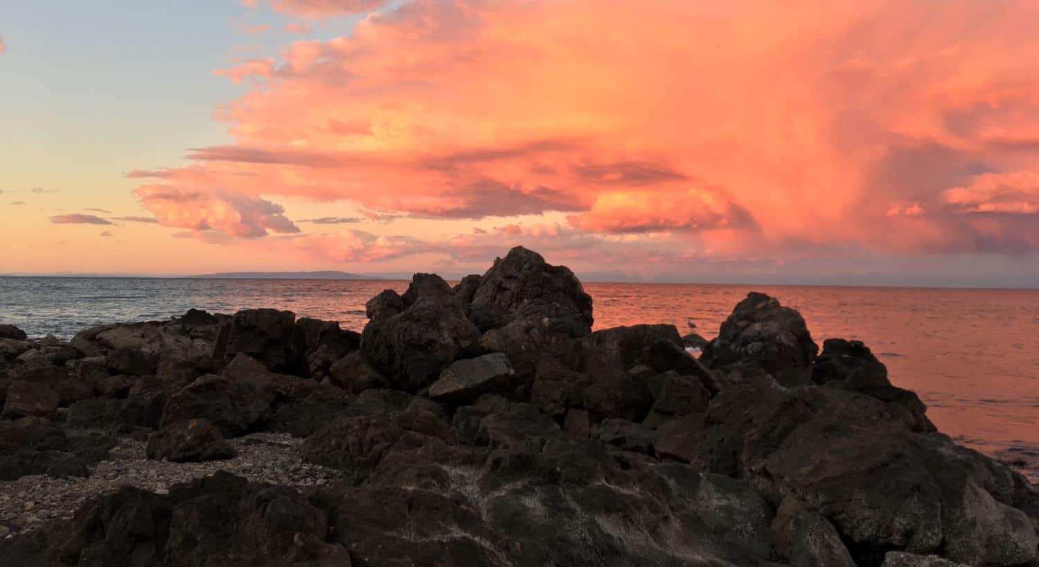 Large rocks with the ocean and pink colored clouds in the background