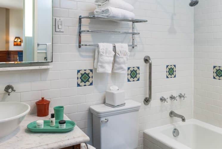 Bathroom with white-tiled walls, white sink, mirror, and tub/shower combo