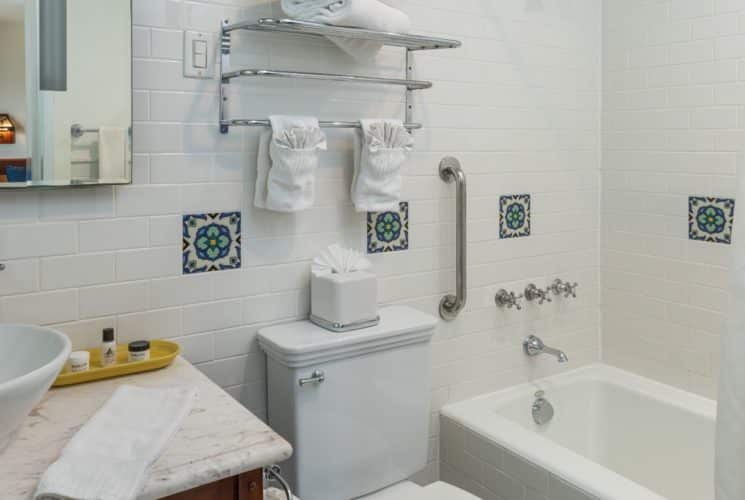 Bathroom with white-tiled walls, white sink, mirror, and tub/shower combo