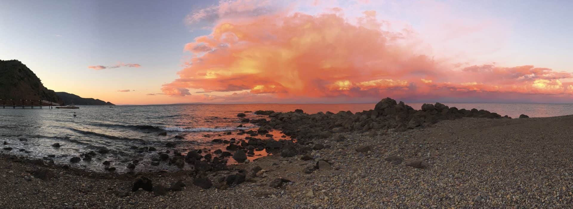 Beach with large rocks and pink colored clouds in the background